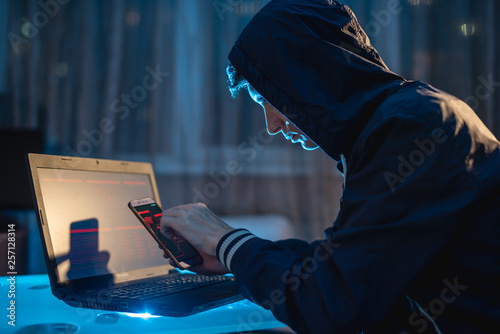 Foto Male hacker in the hood holding the phone in his hands trying to steal access databases with passwords