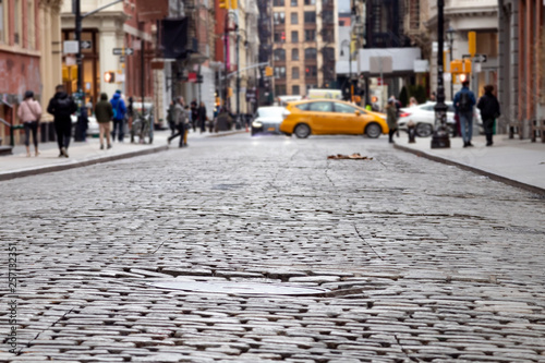 Cobblestone street view of the busy intersection of Broome and Greene Streets with people and taxi in the SoHo neighborhood of Manhattan in New York City