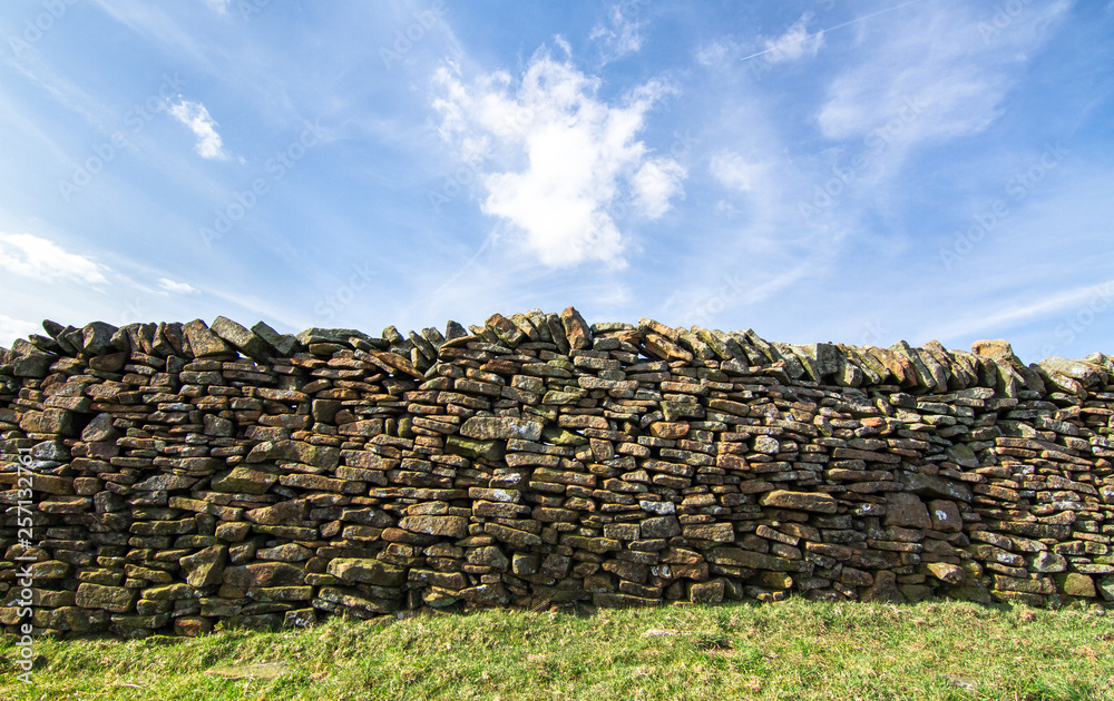Stone wall next to a grassy agricultural field on a sunny day in the Peak District, England.