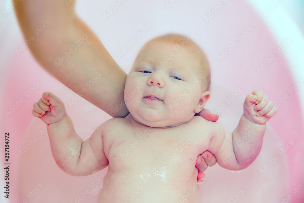 Mom bathes the newborn baby in a pink bathtub, close-up Mom bathes the newborn baby in a pink bathtub, close-up