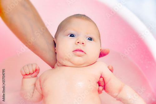 Mom bathes the newborn baby in a pink bathtub, close-up