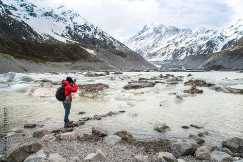 Photographer standing at the edge of Hooker glacier lake with the beautiful view of Mount Cook (3,764 metres) the highest mountains in South Island of New Zealand.
