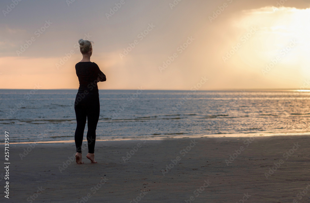 girl is waiting, standing on tiptoe, looking into the distance, barefoot on the sand, sunset on the bay