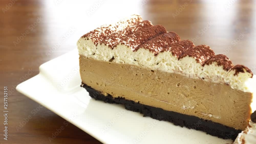 A very slow pan of a slice of tiramisu whip cream sitting on a white plate.