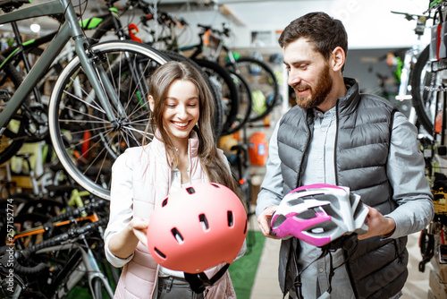 Young woman customer choosing protective helmet standing with salesman in the bicycle shop