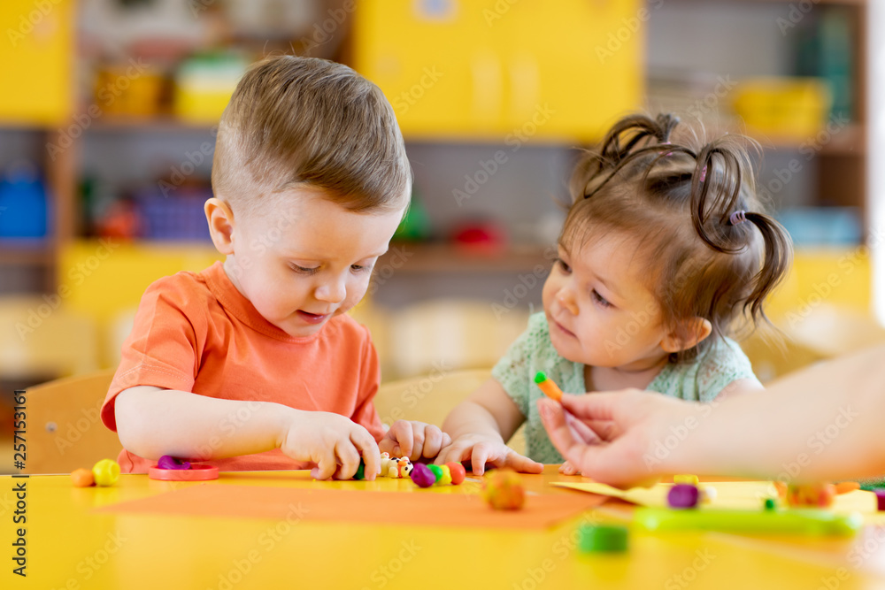 Kids boy and girl play in kindergarten with interest. Children sculpt from plasticine in day care centre.