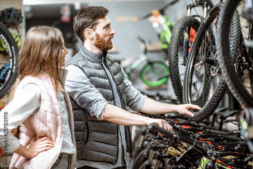Salesman helping young woman to choose a new bicycle to buy standing in the bicycle shop