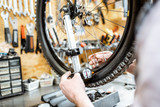 Man aligning bicycle wheel tensing spokes with a special key at the working place of the workshop, close-up view