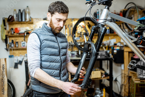 Handsome repairman serving a bicycle, fixing some malfunctions with bicycle fork at the workroom