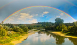 Bright double rainbow in the sky with clouds above the forest and the river