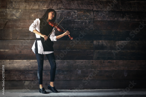 Beautiful woman stand ,hold violin,play music on wooden background, in emotion feeling committed.