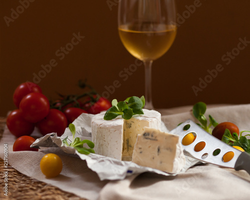 Glass of white wine, tasty starter of french cheese served with green salad and tomatoes on a rustic cloth. Evening light, dark image