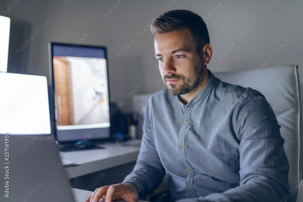 Young serious Caucasian handsome bearded architect sitting in office late at night and finishing project. Young serious Caucasian handsome bearded architect sitting in office late at night and finishing project.