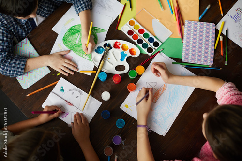 Above view portrait of group of kids drawing pictures sitting at table in art class, copy space