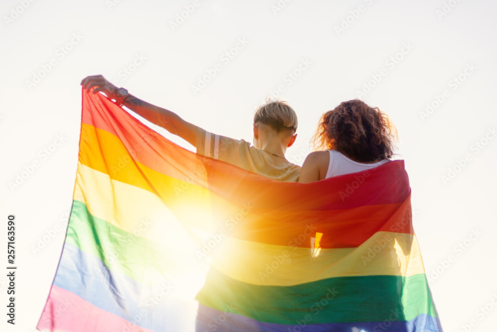 A beautiful lesbian young couple gently lovingly embraces and holds a rainbow flag, equal rights for lgbt community,