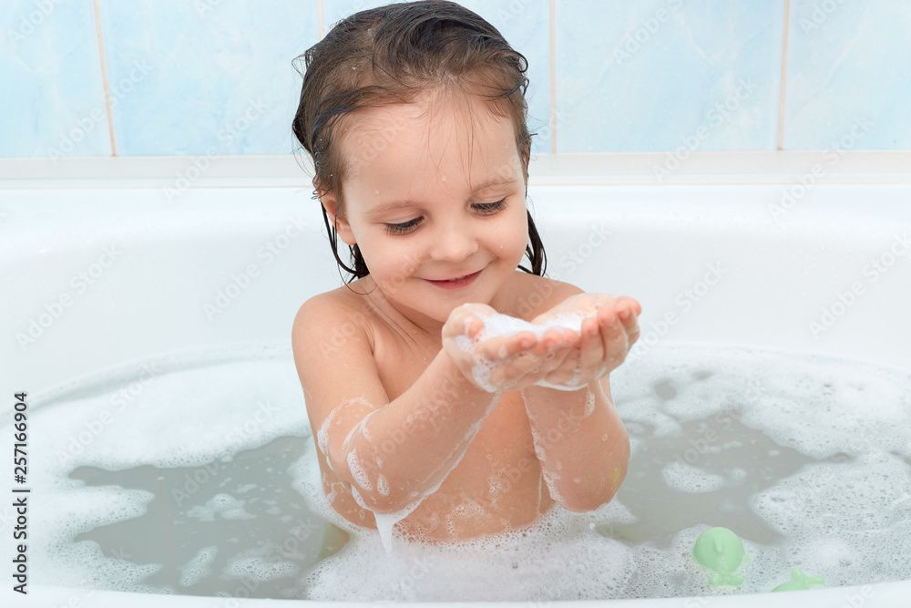 Charming happy baby taking bath, playing with foam bubbles happily