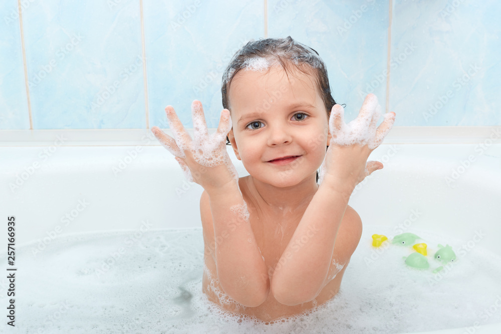 Small adorable child has funny expression, taking bath with plesure