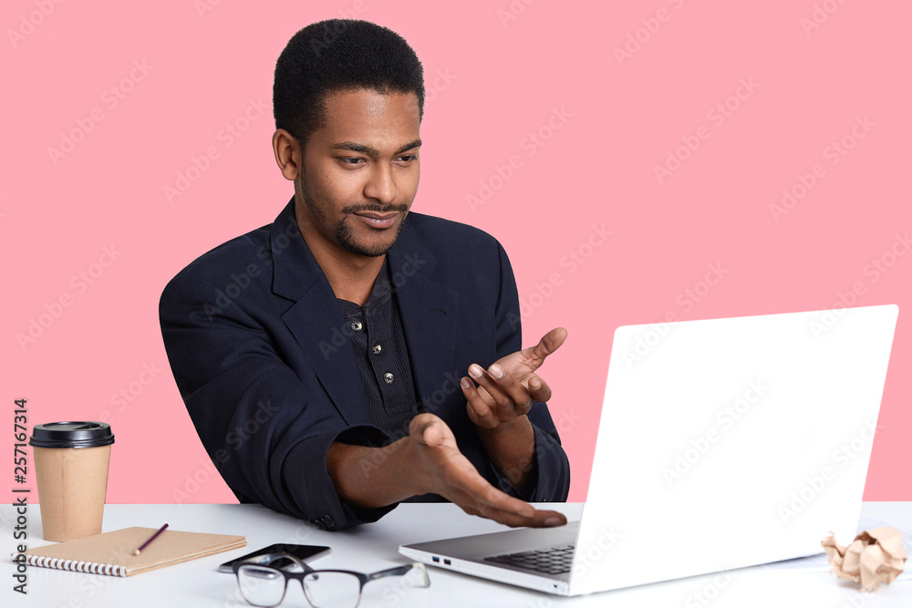Perplexed young business man in black jacket, shows with both hands on lap top monitor, sees arror, do not understend what happened, uses wireless Internet, working online, earns money in office. Perplexed young business man in black jacket, shows with both hands on lap top monitor, sees arror, do not understend what happened, uses wireless Internet, working online, earns money in office.