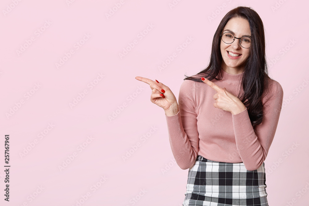 Close up portrait of cute adorable cheerful girl with happy expressions, indicates with fore fingers at blank copy space for your promotional text or advertisement, isolated over pink background. Close up portrait of cute adorable cheerful girl with happy expressions, indicates with fore fingers at blank copy space for your promotional text or advertisement, isolated over pink background.