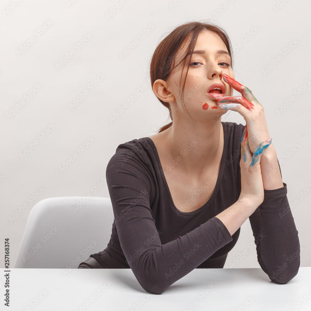 A young attractive brunette girl in black clothes and hands soiled in paint sitting at a table. A young attractive brunette girl in black clothes and hands soiled in paint sitting at a table.
