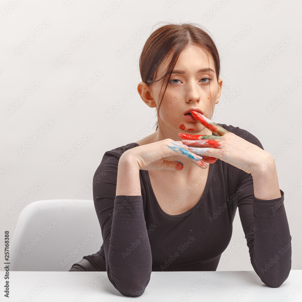 A young attractive brunette girl in black clothes and hands soiled in paint sitting at a table. A young attractive brunette girl in black clothes and hands soiled in paint sitting at a table.