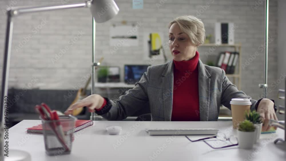 Funny happy young woman singing while listening to loud music in headphones sitting at office desk with laptop surrounded by diverse colleagues, lazy worker wasting time at workplace in co-working