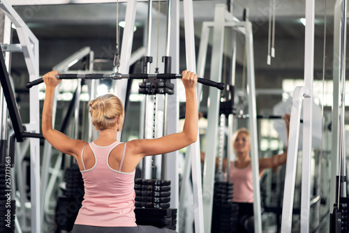 Strong woman exercising with pulldown machine in a fitness club, doing exercises in gym