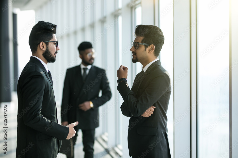 Young asian businessmen have informal meeting in office hall in front of walking collegue Young asian businessmen have informal meeting in office hall in front of walking collegue