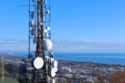 Telecommunications tower, antenna and satellite dish and coastline as background