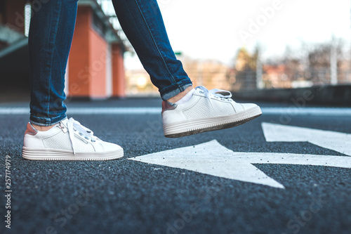 Foto White sneakers on asphalt road with arrow traffic directional sign