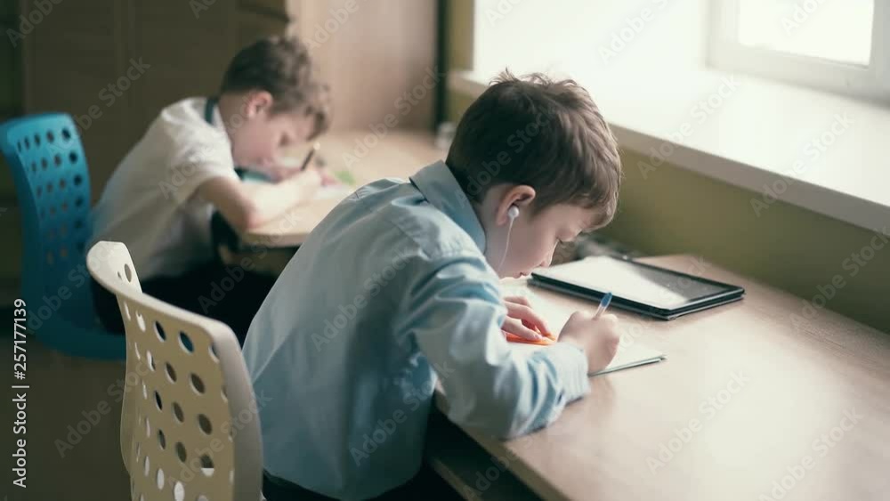Pupils, little boys, do their homework. One of them makes a drawing in a notebook. Pupils, little boys, do their homework. One of them makes a drawing in a notebook.