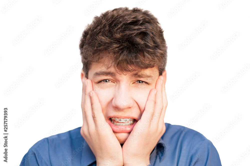 The teenager has a headache as he has braces on his teeth. A boy holds his hands behind his head and suffers The teenager has a headache as he has braces on his teeth. A boy holds his hands behind his head and suffers