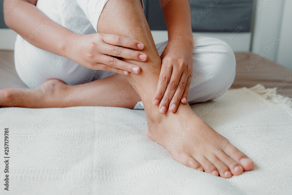Close-Up of Woman Hands is Massaging Her Ankle on Bedroom, Young Adult having Legs Ache After Home Work. Healthcare and Medicine Concept.