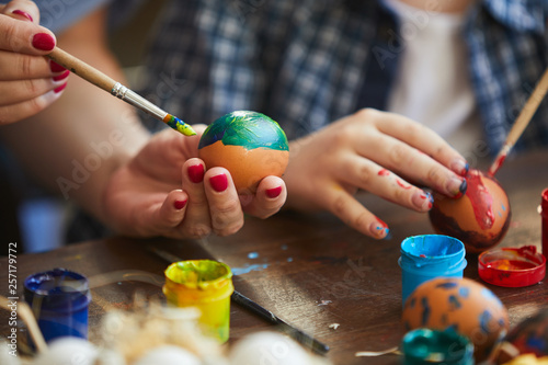 Closeup of child painting Easter eggs with mother, copy space photo