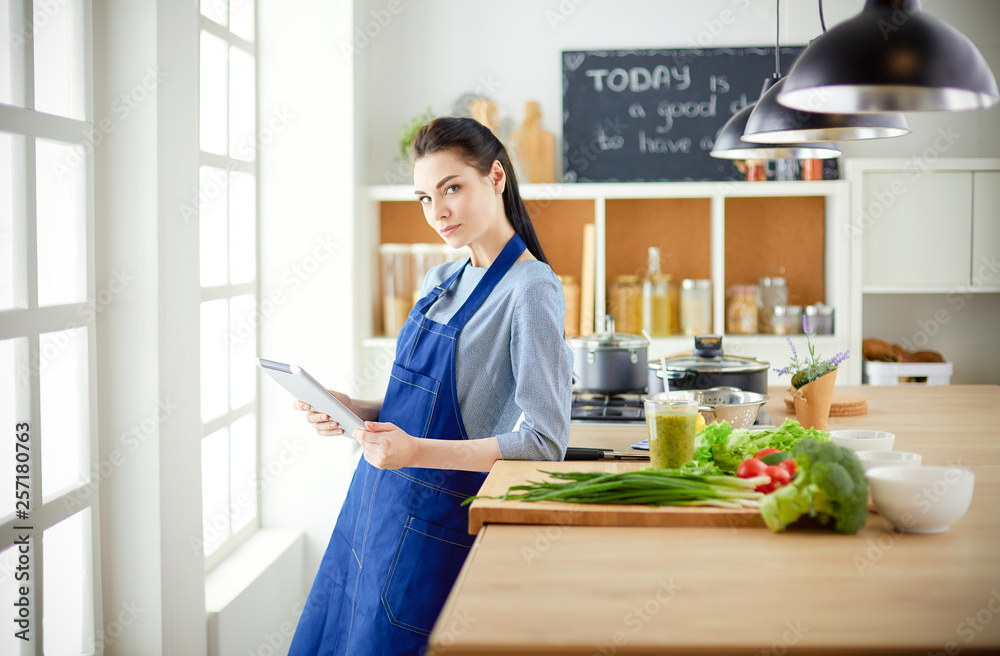 Young woman using a tablet computer to cook in her kitchen