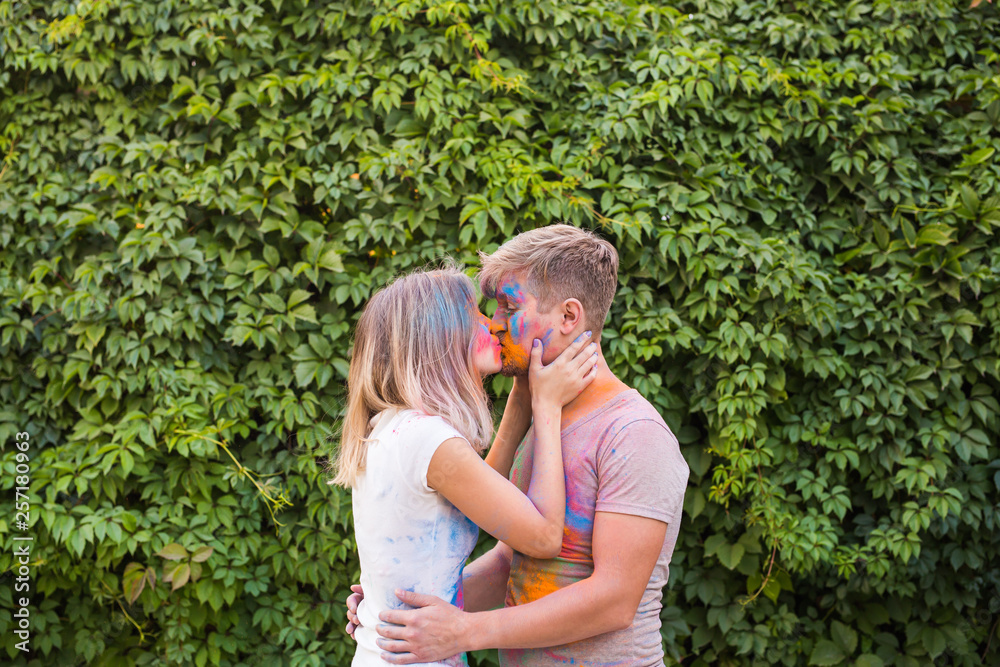 Obraz premium Holiday, holi and people concept - Love couple having fun and kissing covered in paint