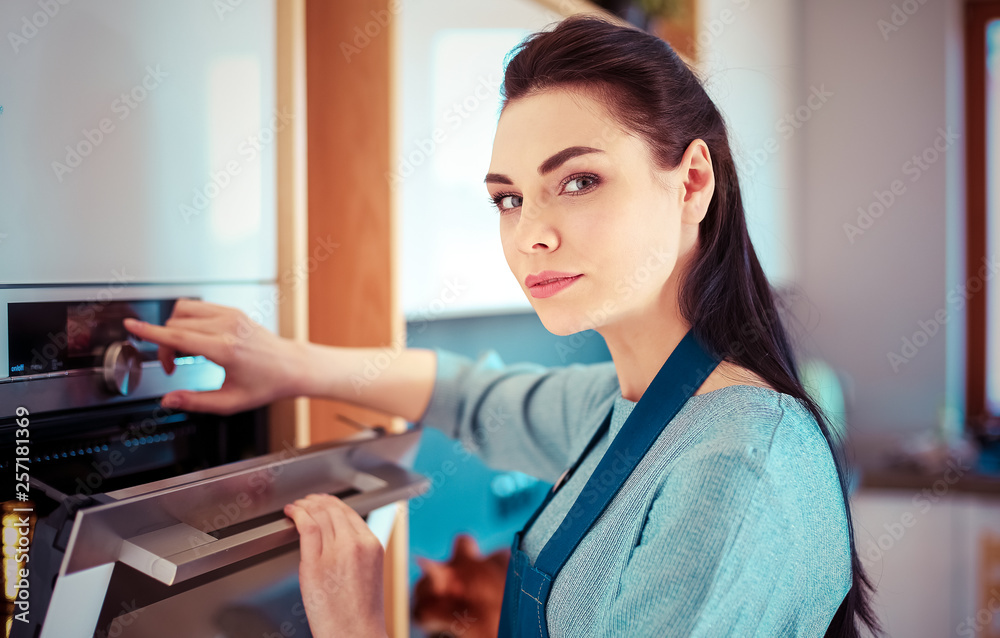 Beautiful young woman checking how her cake is doing in the oven Beautiful young woman checking how her cake is doing in the oven