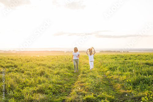 Family, summer and holiday concept - Mother holding her daughter's hand running in green field