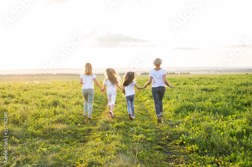 Family, summer and holiday concept - Group of women and girls going away in green field