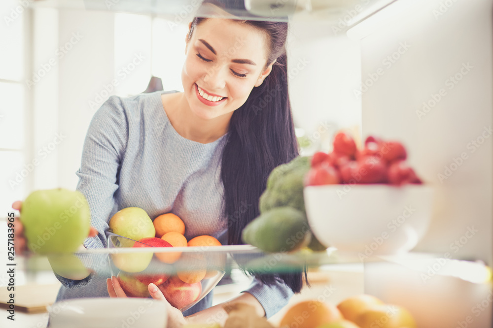 Smiling woman taking a fresh fruit out of the fridge, healthy food concept Smiling woman taking a fresh fruit out of the fridge, healthy food concept