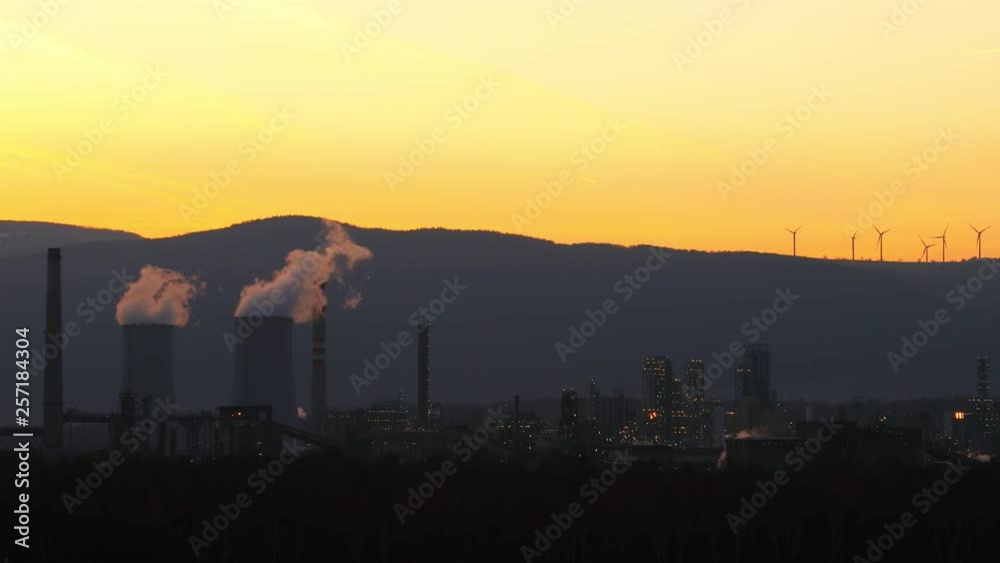 Smoking factory chimneys in sunset with wind turbine. Energy power stations, chemical factories and wind power stations. Global pollution concept, energy consumption. Smoking factory chimneys in sunset with wind turbine. Energy power stations, chemical factories and wind power stations. Global pollution concept, energy consumption.