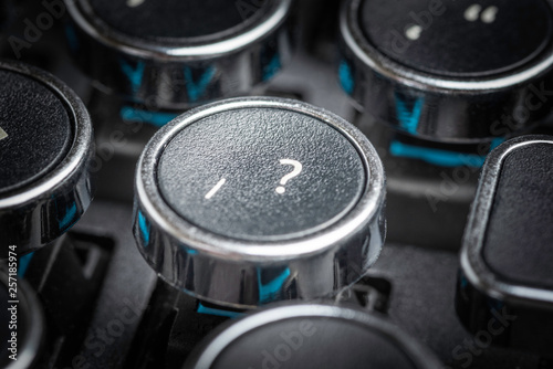 An extreme close-up or macro shot of a round slash and question mark symbols key on a vintage-inspired retro-style clicky black-and-silver metal typewriter keyboard. © Dominique James