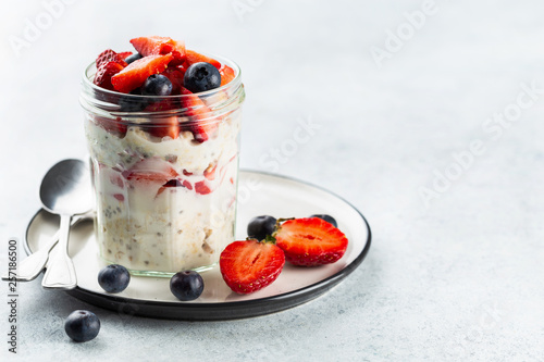 Overnight oats with chia seeds and fresh strawberries and blueberries in a glass jar. Healthy breakfast.