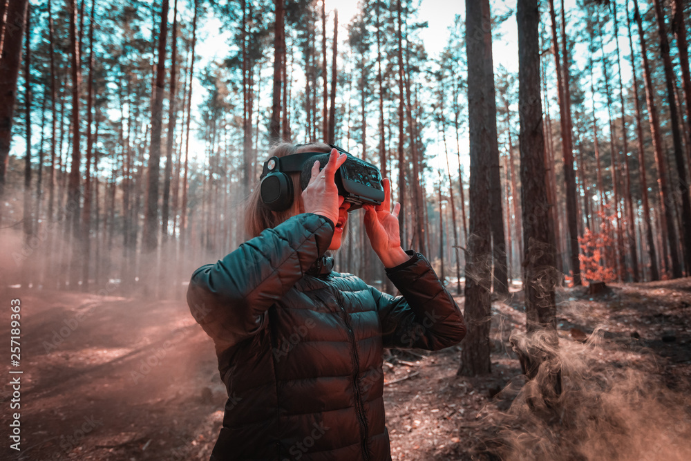Woman in forest with virtual reality headset looking straight with orange smoke from smoke bombs Woman in forest with virtual reality headset looking straight with orange smoke from smoke bombs