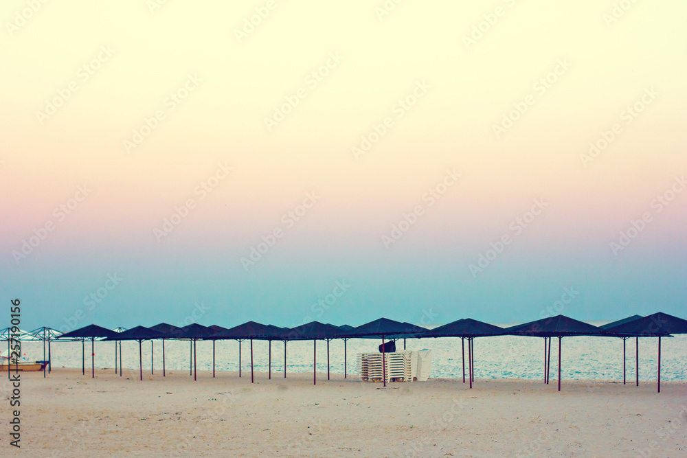 Empty beach, beach umbrellas and beautiful sunset. Romantic atmosphere.