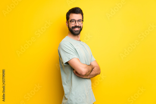 Man with beard and green shirt keeping the arms crossed in lateral position while smiling