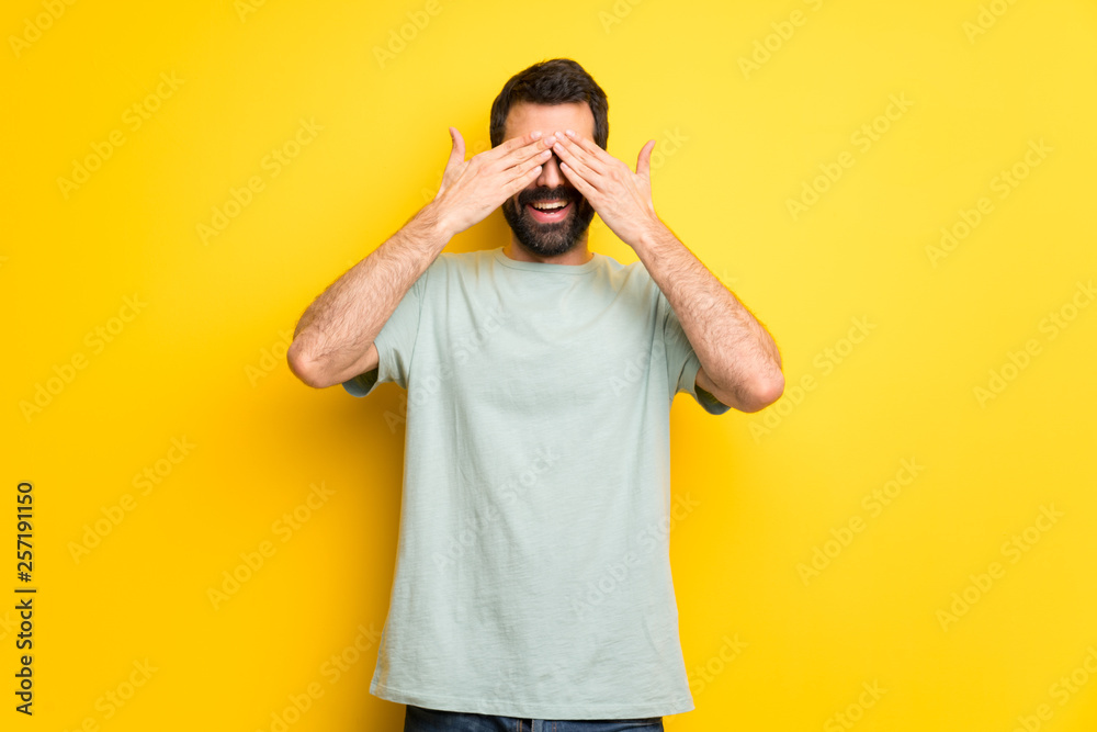 Man with beard and green shirt covering eyes by hands. Surprised to see what is ahead Man with beard and green shirt covering eyes by hands. Surprised to see what is ahead
