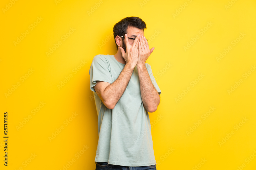 Man with beard and green shirt covering eyes by hands and looking through the fingers Man with beard and green shirt covering eyes by hands and looking through the fingers
