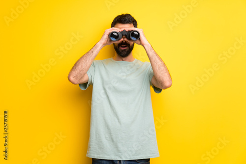 Man with beard and green shirt and looking in the distance with binoculars