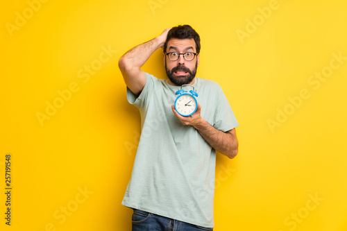 Man with beard and green shirt restless because it has become late and holding vintage alarm clock